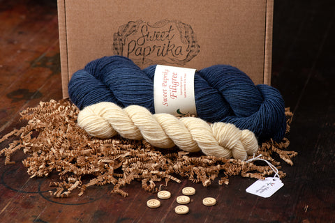 The contents of the Kinsfolk Cardigan kit presented in front of a kraft box with the Sweet Paprika logo stamped on it