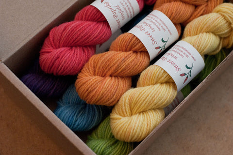 A set of six mini-skeins of Winfield yarn in rainbow colours presented in a cardboard box