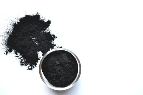Active charcoal powder in a jar and spread across a white background