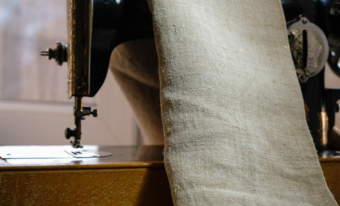 An old fashioned sewing machine with a piece of hemp fabric draped over the top of the machine. 