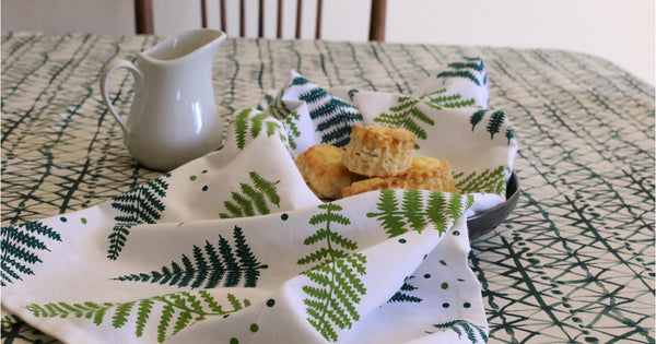A white tea towel with ferns printed in two shades of green.
