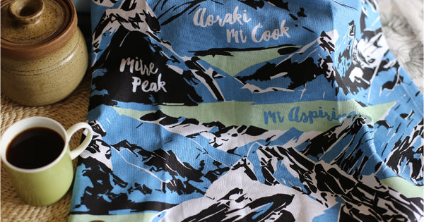 A blue, mint and black print of New Zealand mountians on a white tea towel.