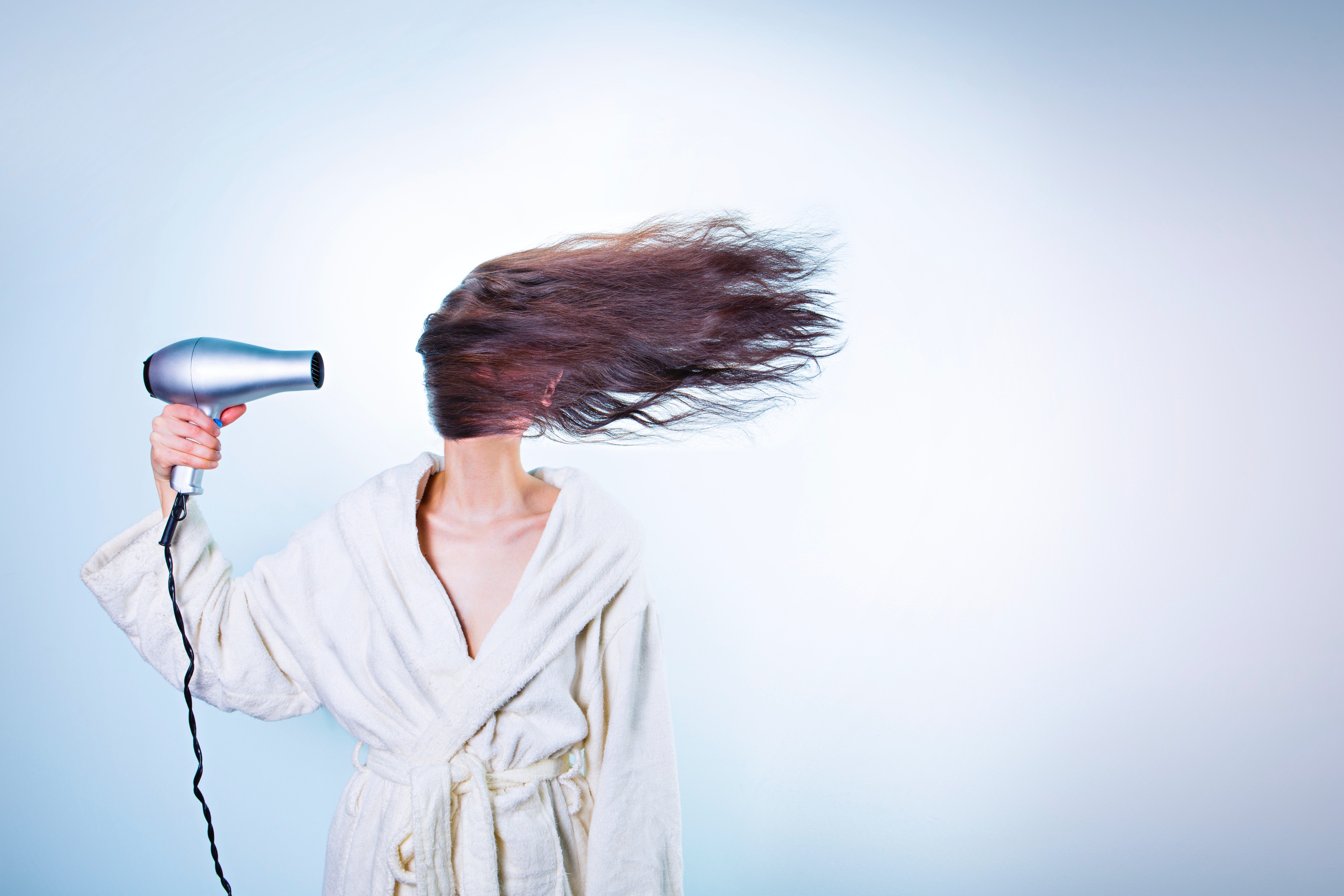 Woman using a hair dryer - heated styling tools damage hair growth