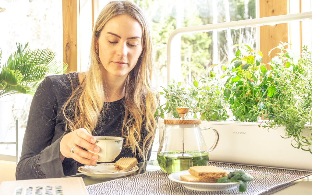 Woman drinking tea beside a window and a Click and Grow smart garden 9.