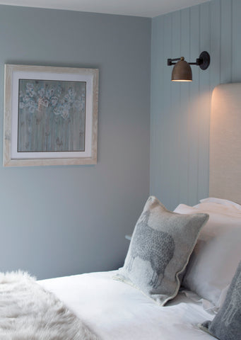 A bedroom with a pale blue wall and hanging art