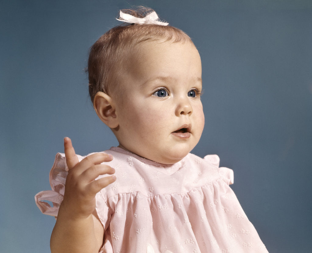 1960s baby girl wearing pink dress with a bow in her hair 