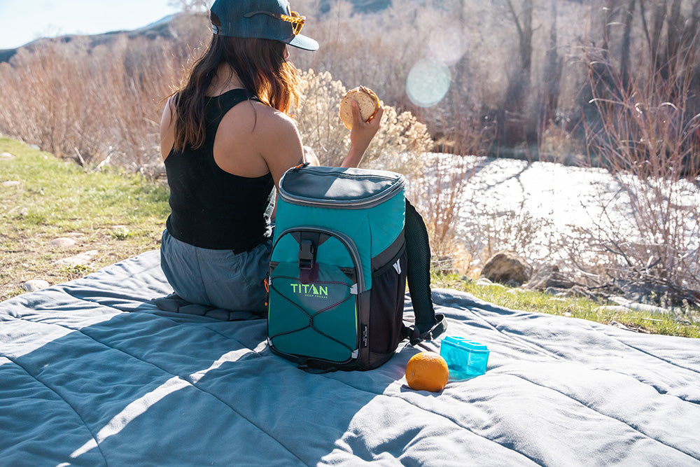 Girl enjoying an outdoor picnic with a Titan Deep Freeze® 24 Can Backpack Cooler beside her