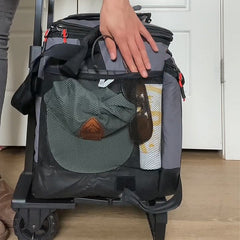 Person loading mesh side pockets of wheeled cooler with hat, sunglasses & sunscreen