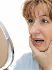 woman looking in mirror and noticing face is beginning to sag