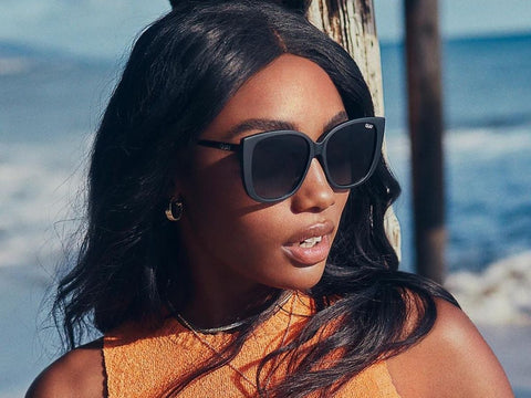 A female model on the beach wearing an orange top and EVER AFTER oversized sunnies