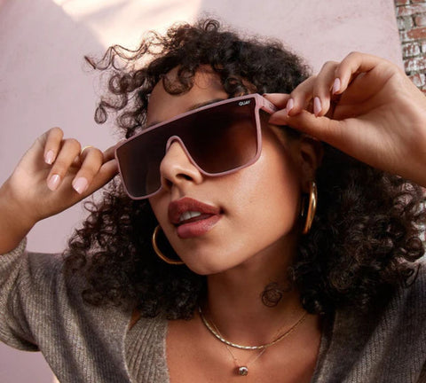 A female model posing in front of a pink wall wearing QUAY NIGHTFALL sunnies