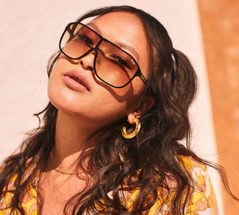 A female model posing wearing a festival outfit with QUAY STILL RICH sunnies