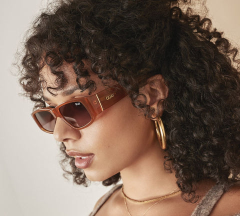 A side profile of a female model wearing QUAY NO ENVY brown sunglasses