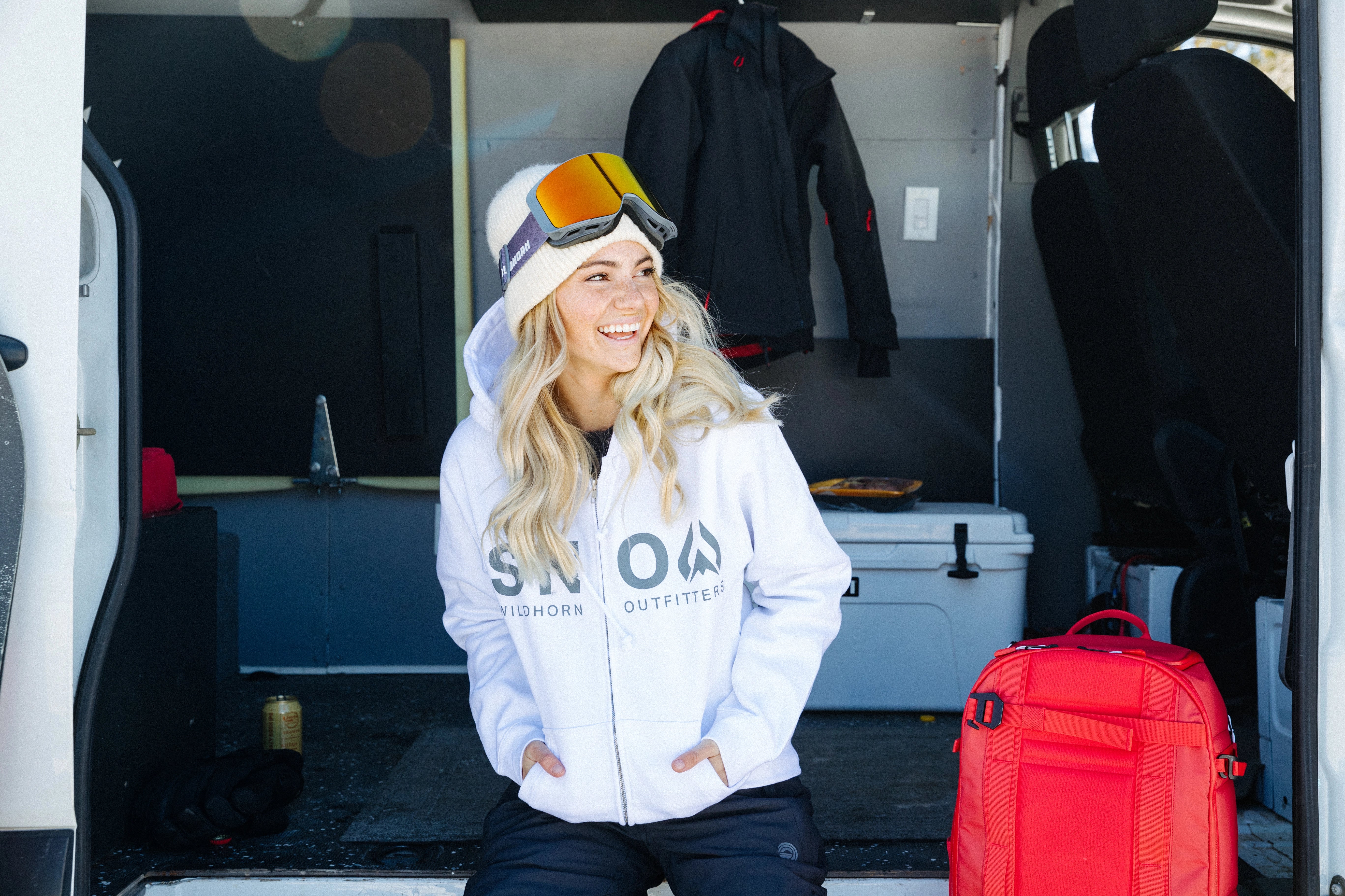 Woman in the back of a van smiling with ski goggles on her head