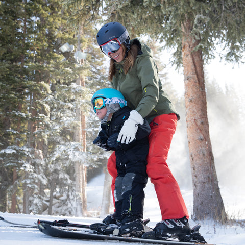 mom helping her son learn to ski while both of them wear ski helmets required at ski resorts
