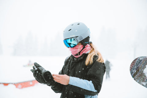 A woman putting on snow gloves while wearing a Wildhorn ski helmet that’s compulsory