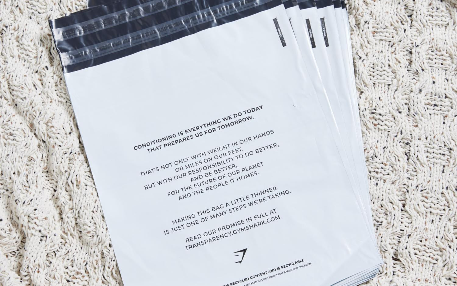 ภาพถ่ายขากมุมบนของถุงไปรษณีย์พลาสติกสีขาวพร้อมข้อความสั้นๆ เกี่ยวกับความยั่งยืน