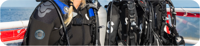 Person in scuba gear on a boat, surrounded by additional diving equipment.
