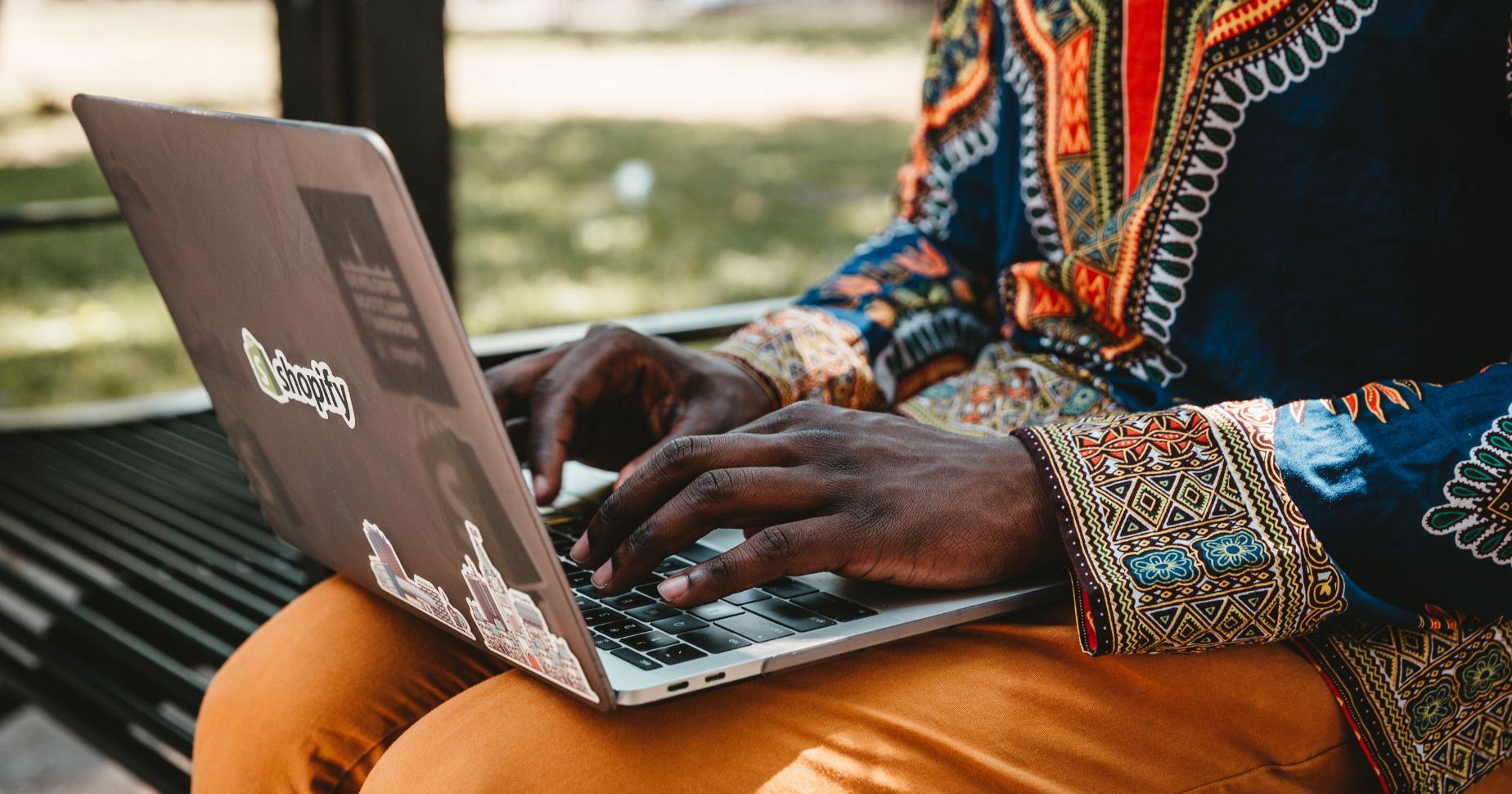 En man som sitter på en parkbänk och registrerar ett domännamn på sin laptop: domänregistrator