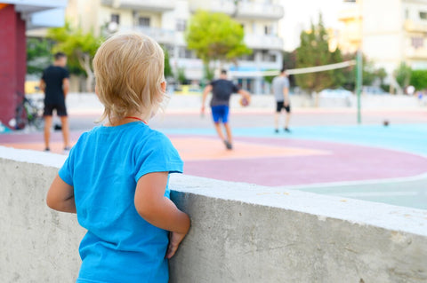 boy watching people play basketball from the sidelines