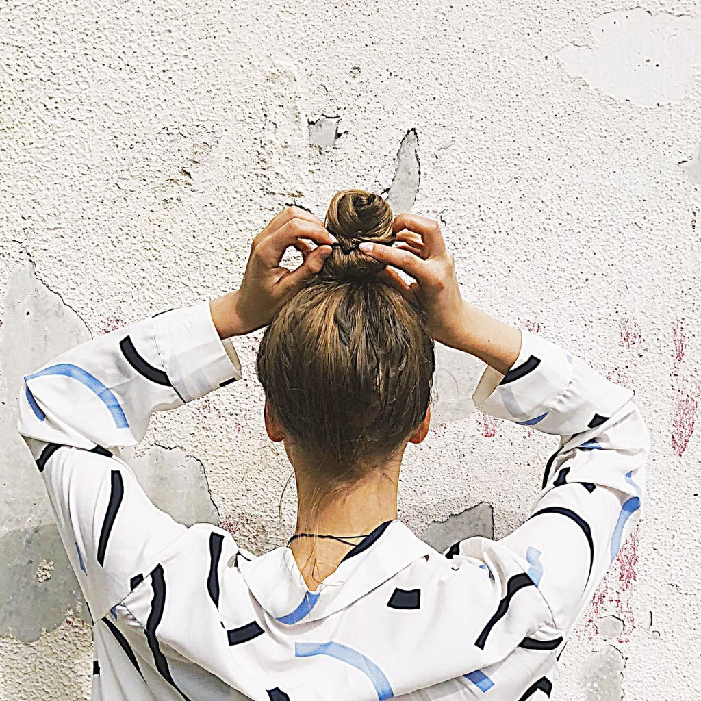 Woman in white and black abstract jumper facing a wall and styling her hair