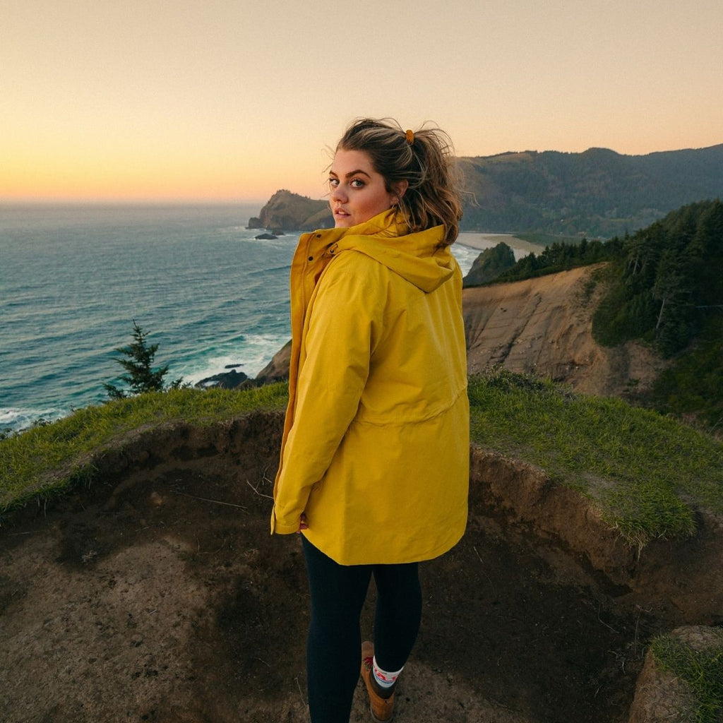 Woman in yellow raincoat standing on top of a cliff for staycation essentials