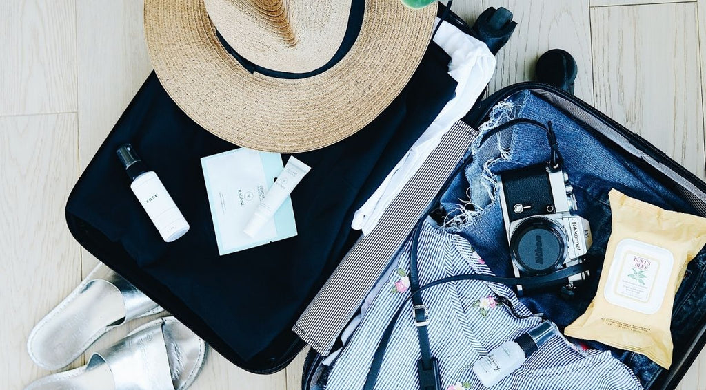 Open suitcase for staycation essentials with clothes, straw hat and camera