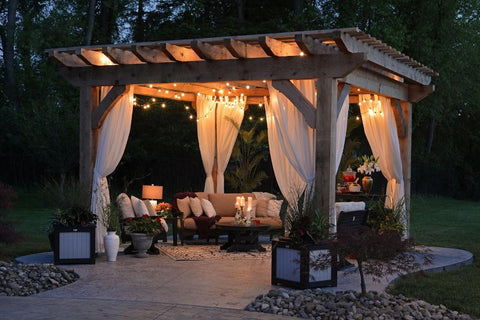 Outdoor setting with a pergola and seating; sofa and chairs under lights with white drapes