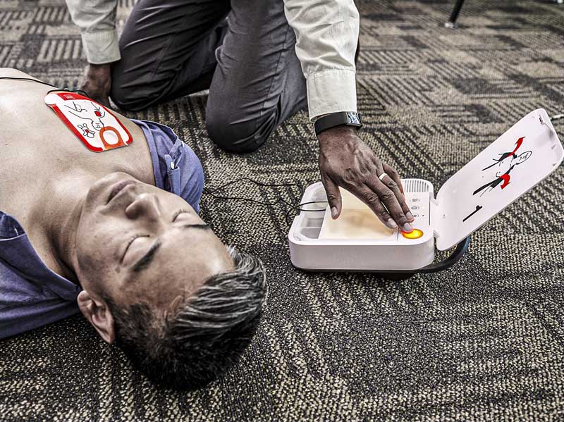 Man on ground unresponsive with pads attached to chest while woman presses the shock button on a LIFEPAK CR2 AED