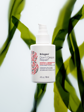 Don't Despair, Repair! Moisture + Damage Defense Leave-In Treatment in front of green leaves