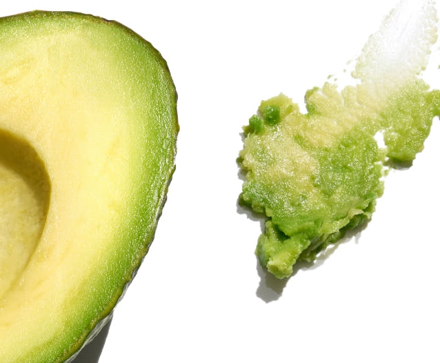 Halved avocado beside mashed avocado on a white background. 