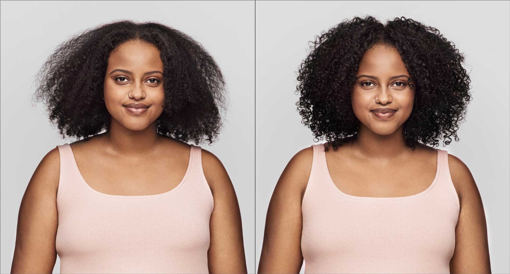 Woman with very curly hair wearing pink tank top in front of grey background with frizzy hair and defined curls. 