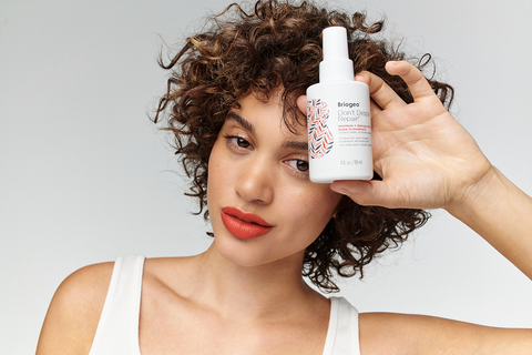 Woman with short, brown curly hair holding Don't Despair, Repair! Moisture + Damage Defense Leave-In Treatment