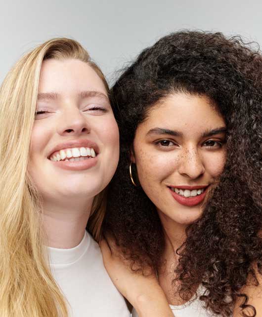 A blonde woman and a dark-haired woman smiling next to each other