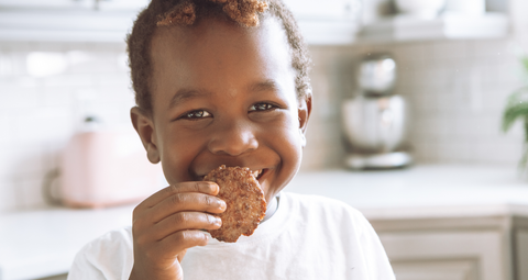 image of a young boy in a kitchen, smiling holding a cookie