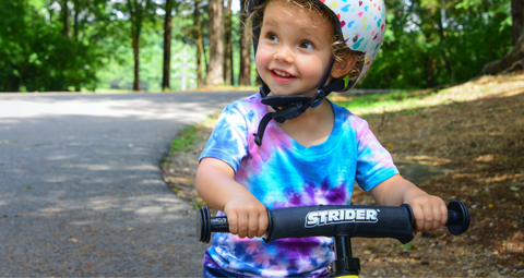 bild av en leende ung pojke som håller på sin cykel med hjälm.