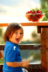 image of a happy young boy looking over his shoulder, mouth wide open. In front of him on a ledge is a bowl of strawberries