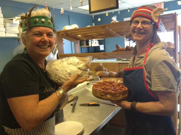 2 Old Village Bakery employees smile at the camera holding bread and cake