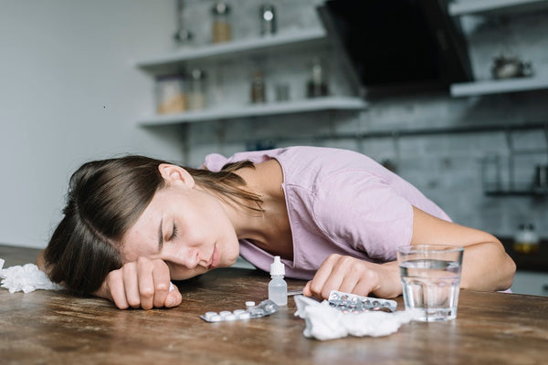 unhealthy women lying on desk with pills everywhere- jeangeniehealth