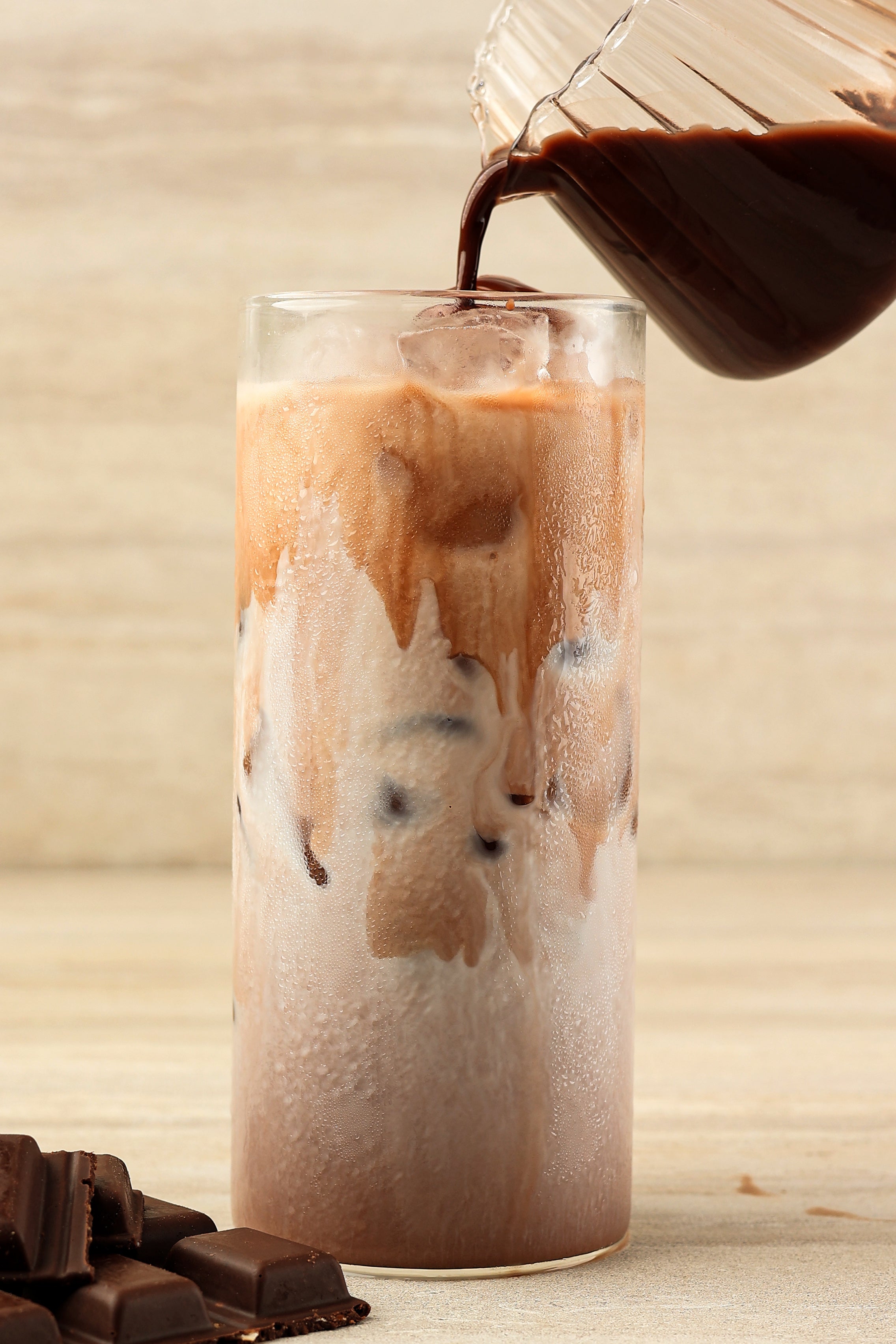Velvety iced drinking chocolate being poured into a tall glass over ice
