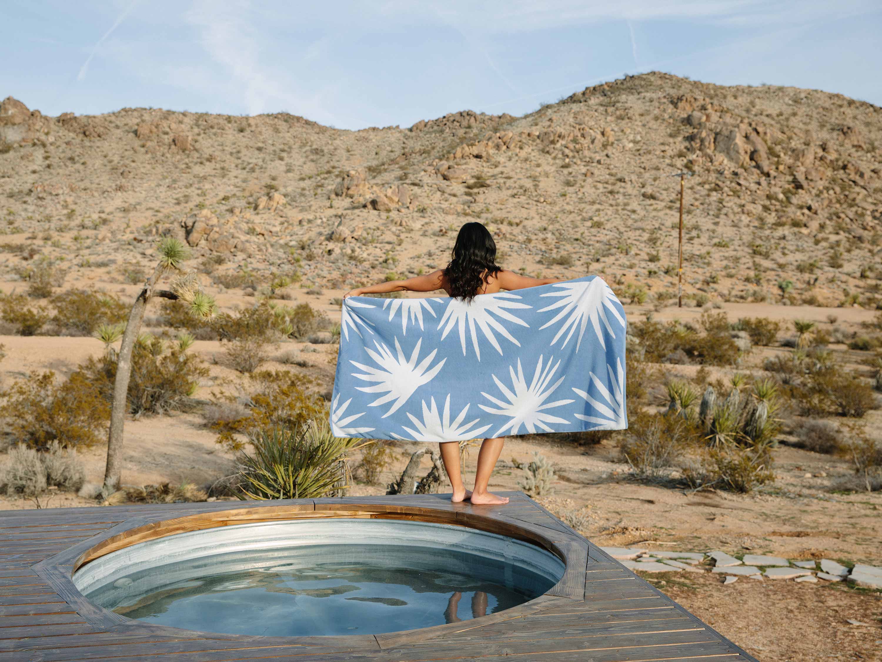 A woman holding a blue agave print Cabana towel by a jacuzzi.
