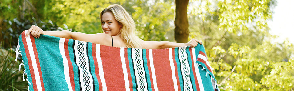 A woman holding a Mexican Blanket in front of trees.