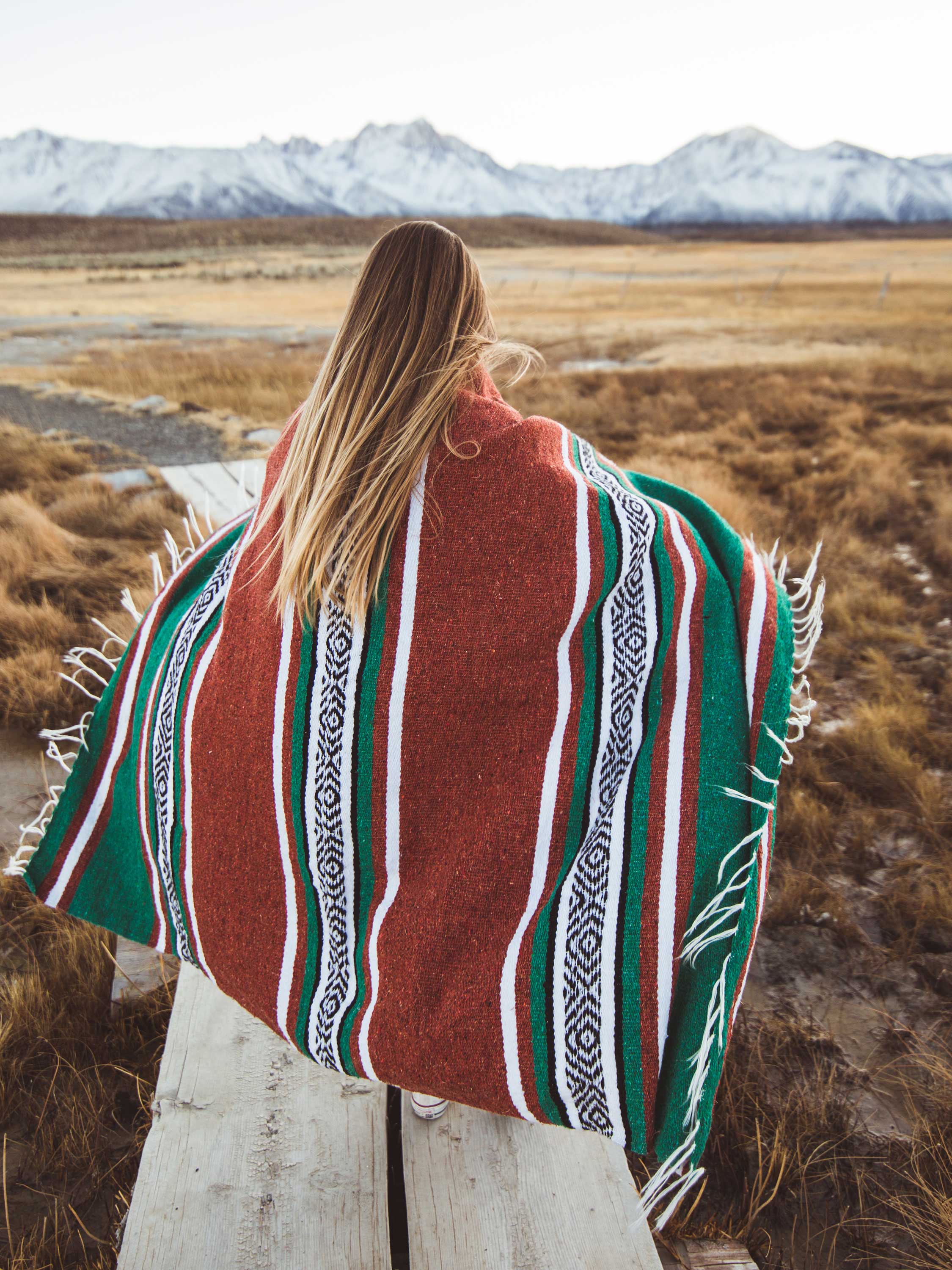 A woman walking towards mountains draped in a Mexican Blanket.