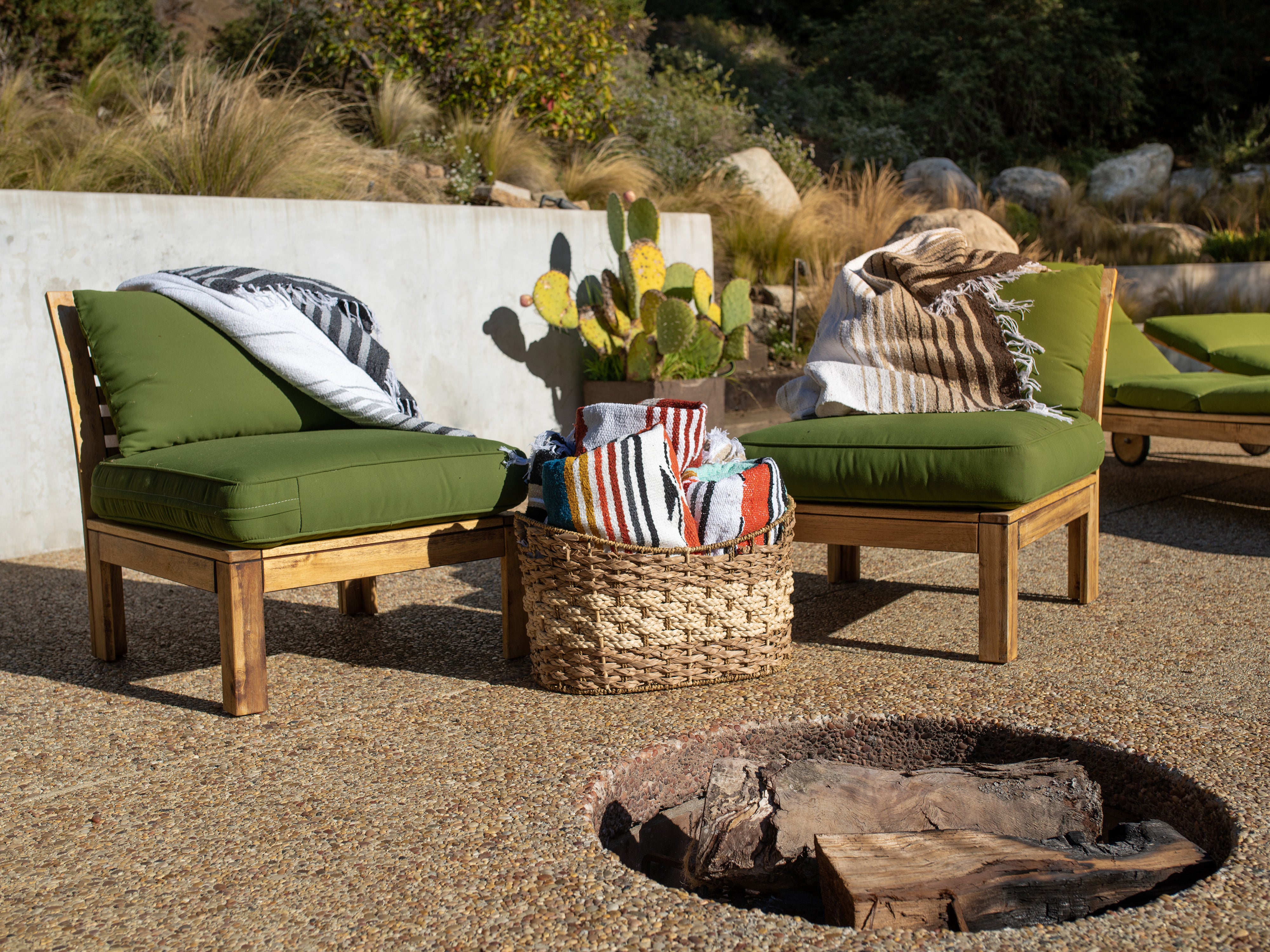 A pair of green chairs with a Mexican Blanket draped over them next to cactus.