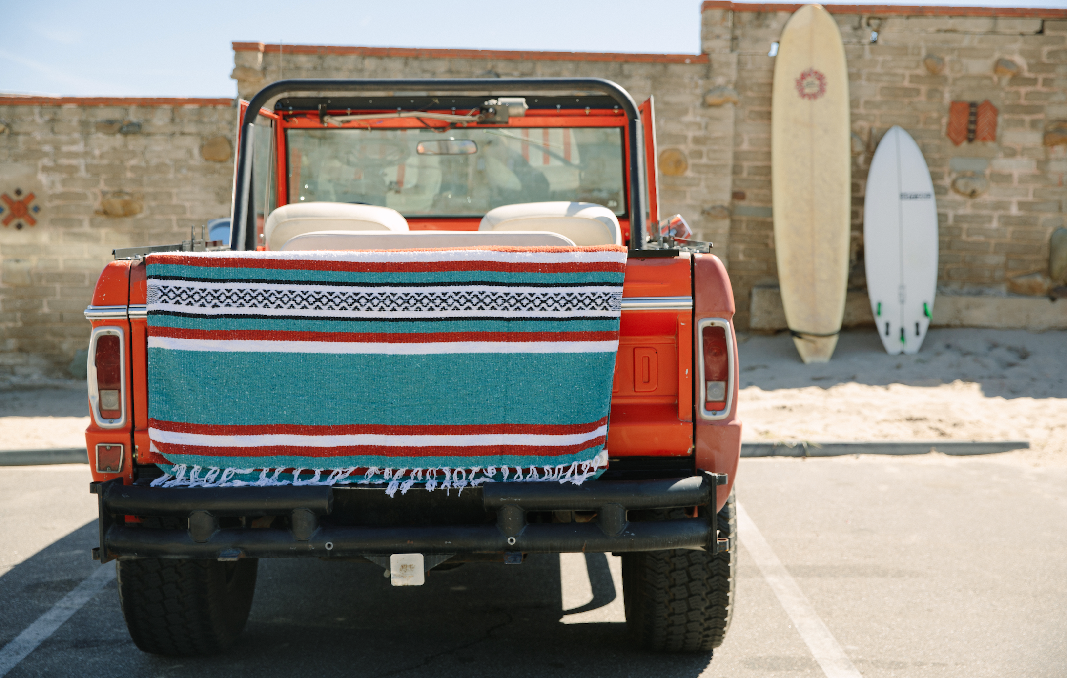 A Mexican blanket draped over the back of a vintage Bronco car. 