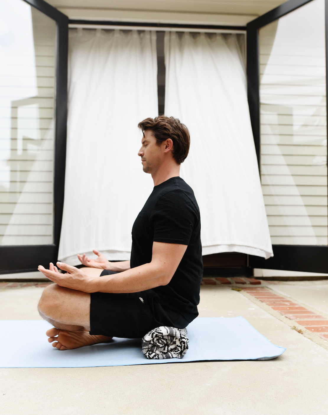 A man sitting on a yoga mat towel doing yoga. 