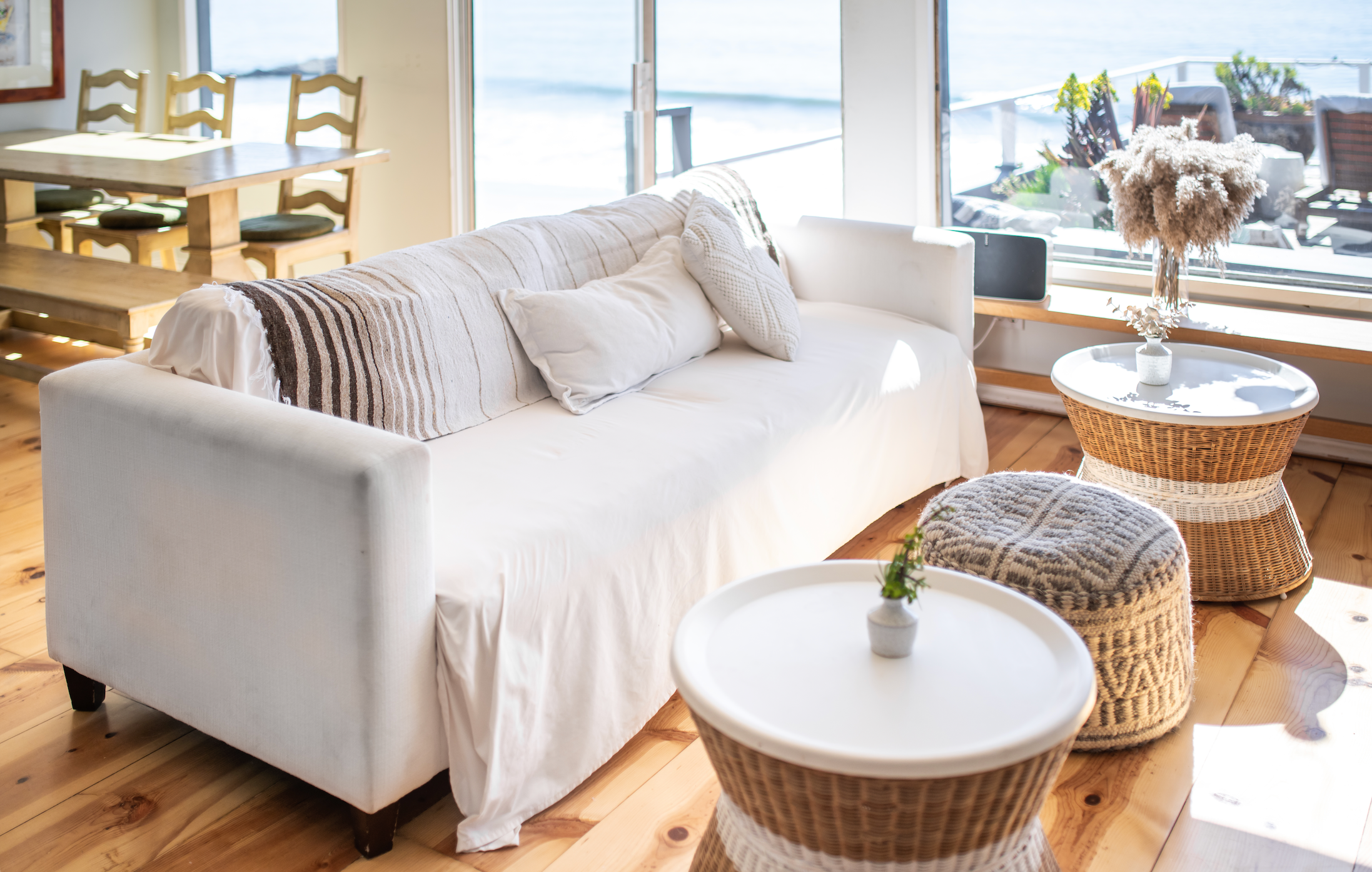 A photo of a couch next to a window looking out to the beach.