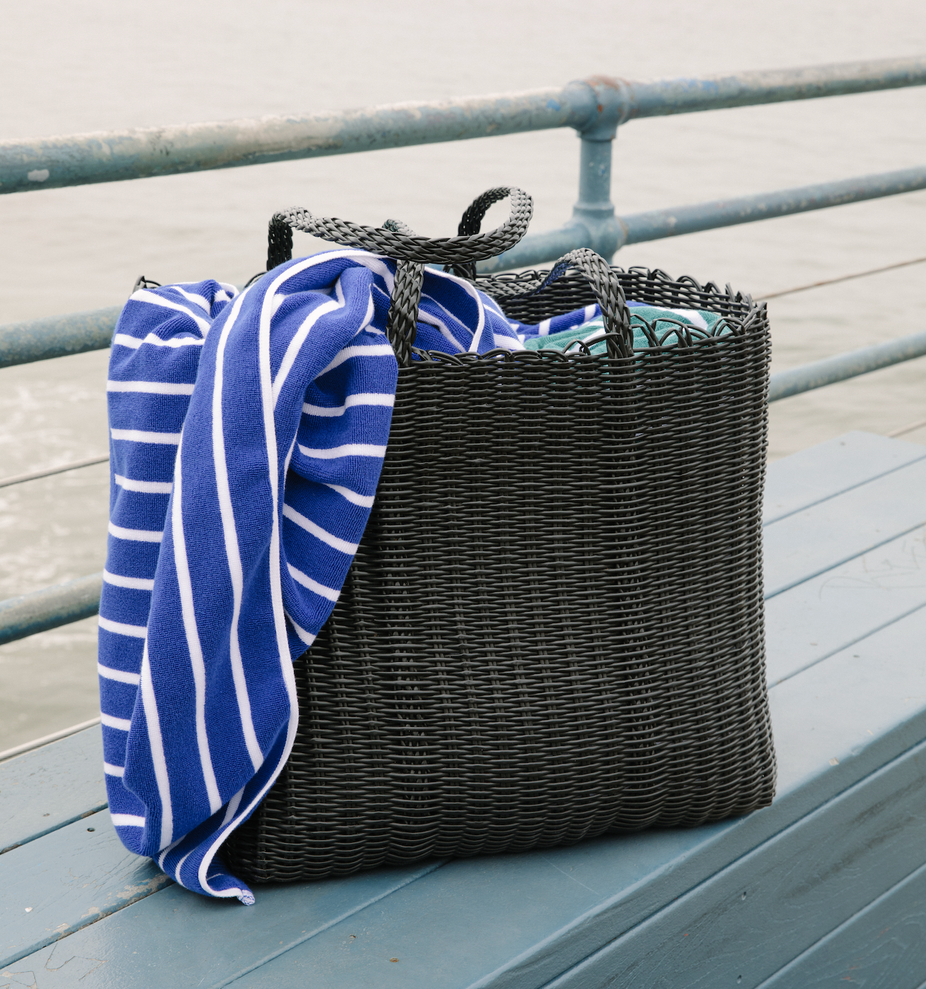 A black woven beach bag with a blue striped towel in it.