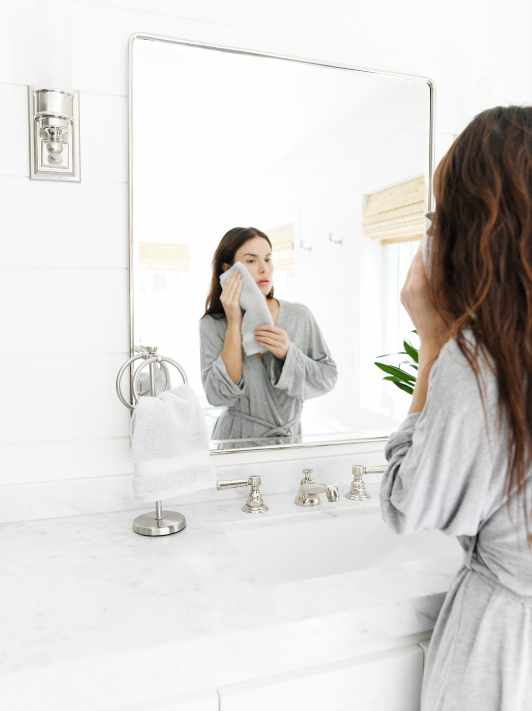 A woman patting her face in the mirror with a cotton face towel.