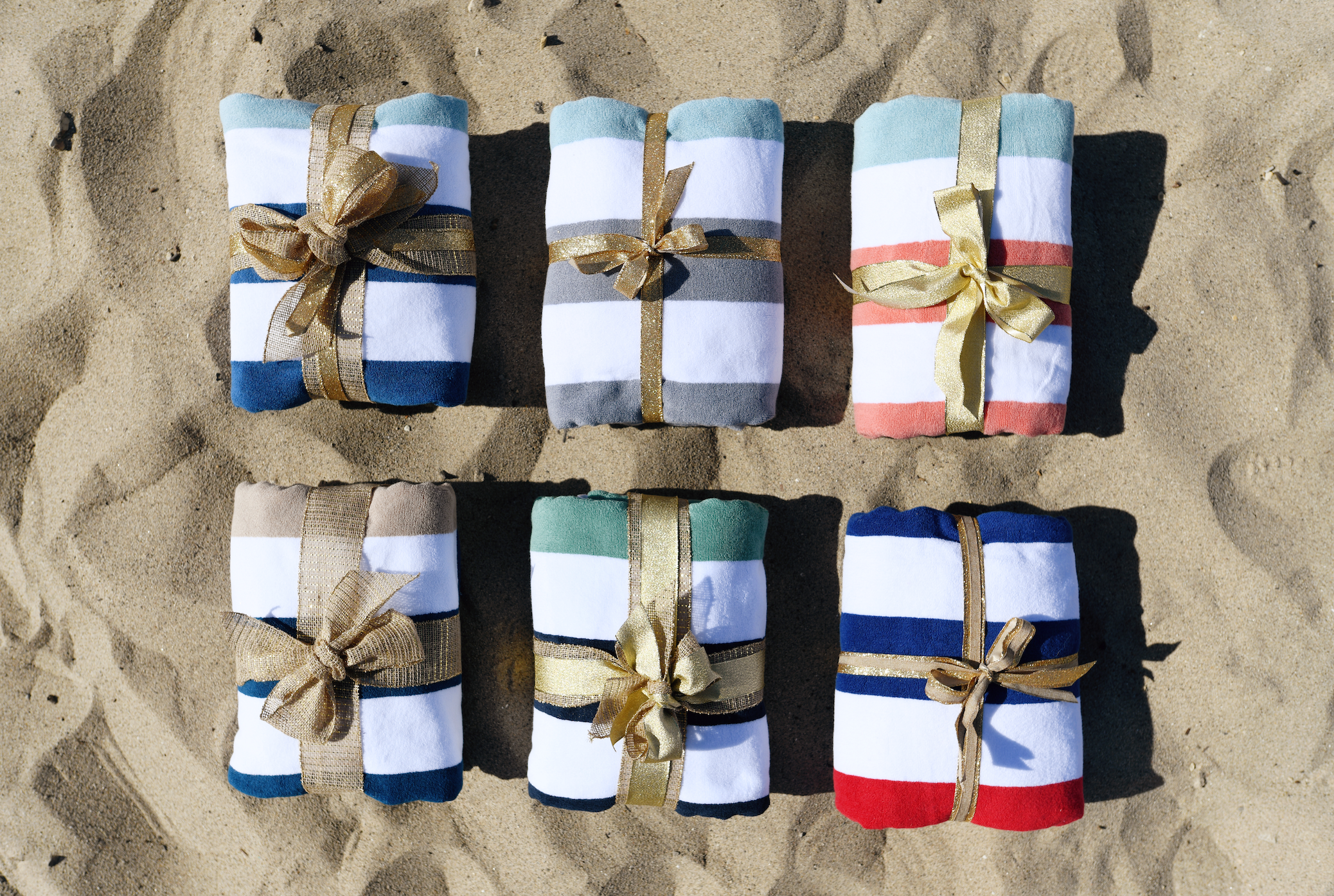Six Cabana towels folded side by side with a ribbon on the sand.